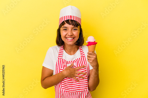 Young mixed race ice cream maker woman holding an ice cream isolated on yellow background laughing and having fun. © Asier