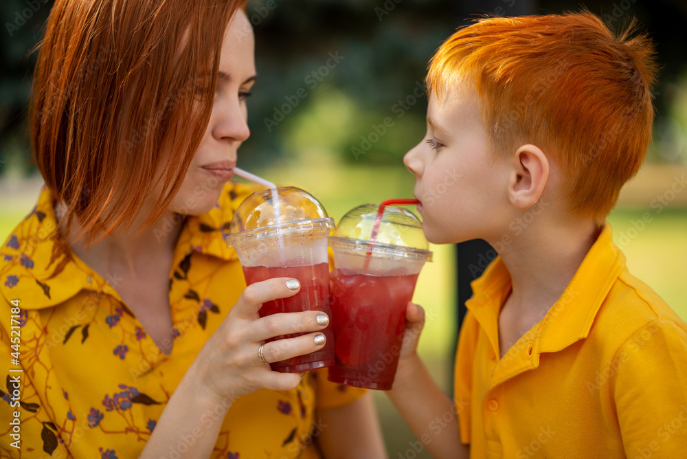 Red-haired young boy and mom are drinking red lemonade. Summer outdoor recreation. Red-haired young boy and mom are drinking red lemonade. Summer outdoor recreation.