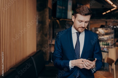 Male investor in blue suit using smartphone in restaurant