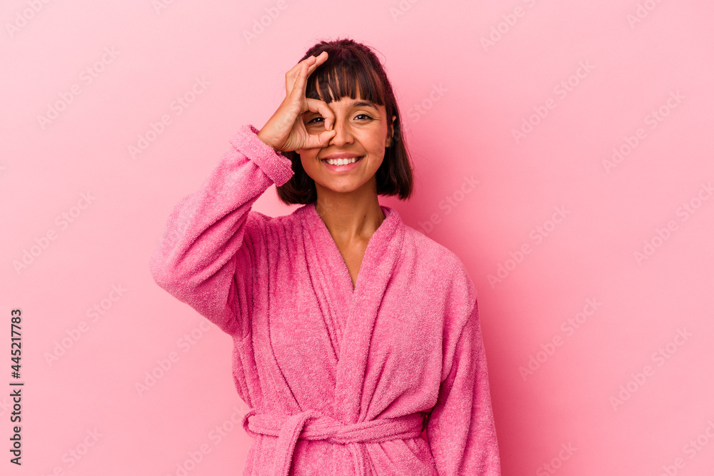 Young mixed race woman wearing a bathrobe isolated on pink background excited keeping ok gesture on eye. Young mixed race woman wearing a bathrobe isolated on pink background excited keeping ok gesture on eye.