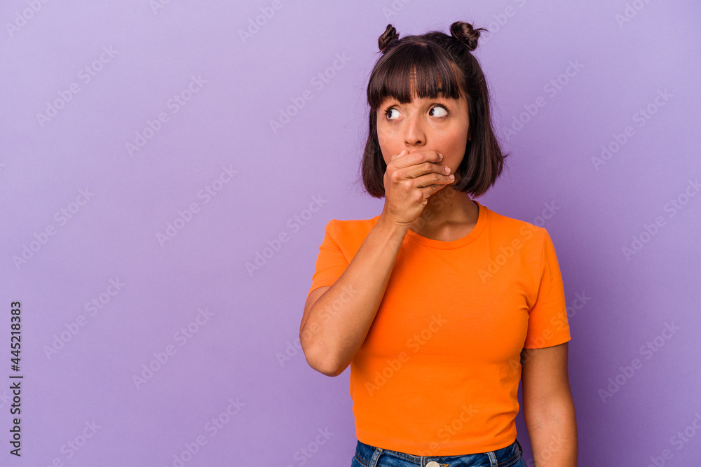 Young mixed race woman isolated on purple background thoughtful looking to a copy space covering mouth with hand. Young mixed race woman isolated on purple background thoughtful looking to a copy space covering mouth with hand.