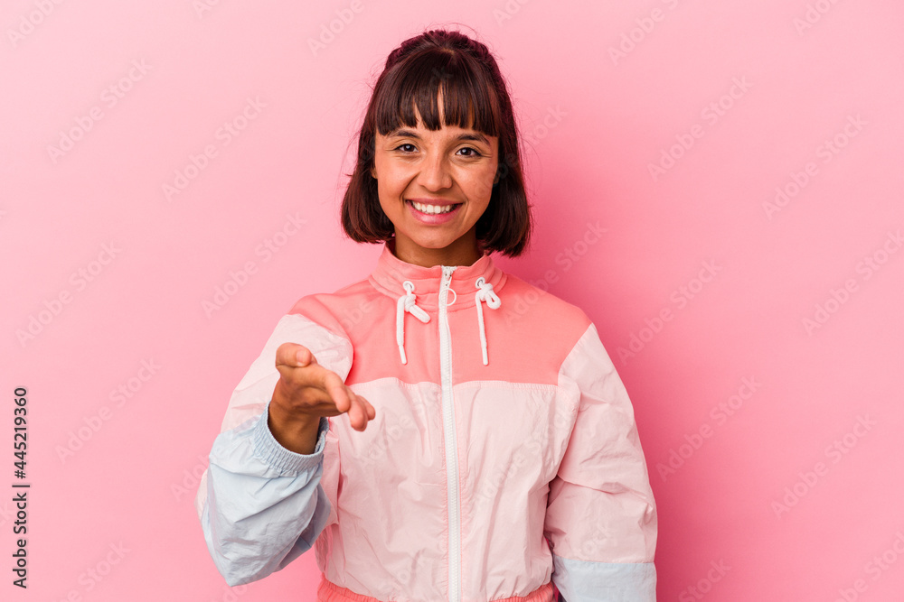 Young mixed race woman isolated on pink background stretching hand at camera in greeting gesture. Young mixed race woman isolated on pink background stretching hand at camera in greeting gesture.