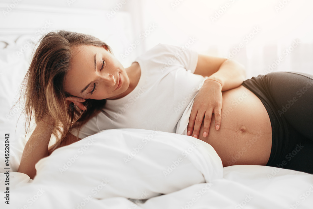Dreamy pregnant woman touching belly in bed Dreamy pregnant woman touching belly in bed