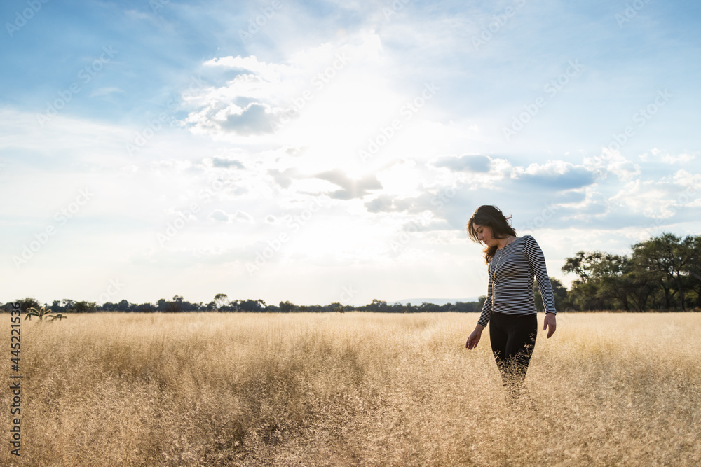 Young adult smiling Mexican woman standing in a dry grassy meadow looking down Young adult smiling Mexican woman standing in a dry grassy meadow looking down