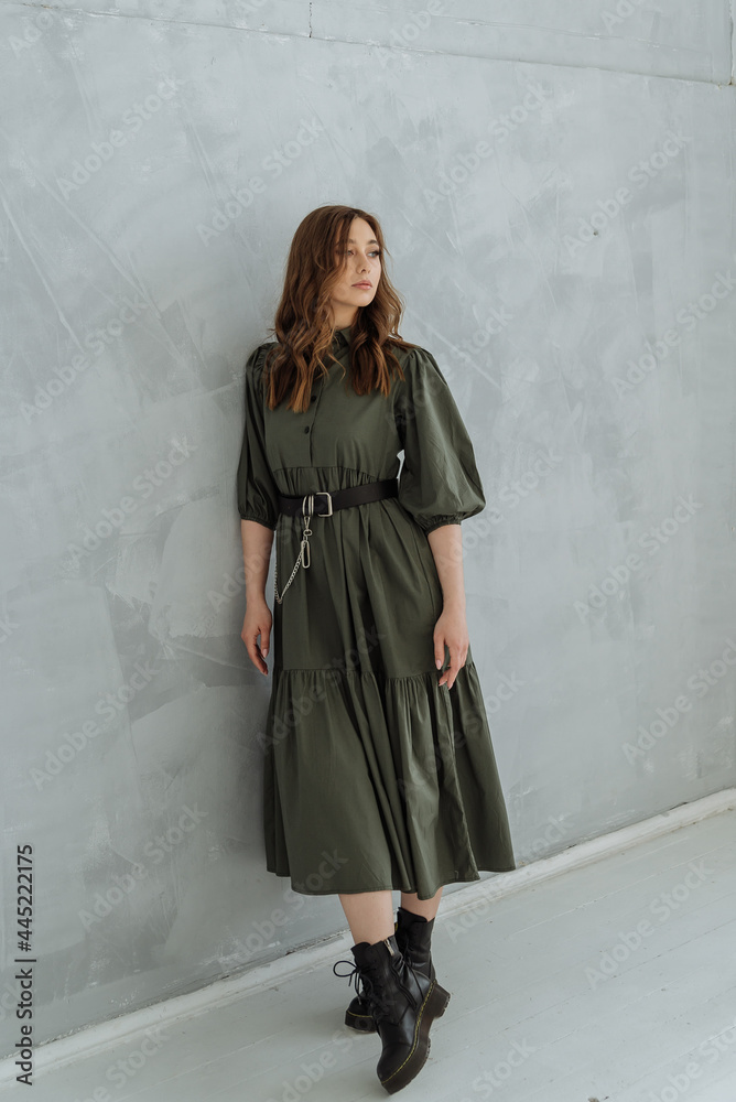 a woman in a green long dress and rough black shoes on a gray background. trending women's fashion clothing 2021.