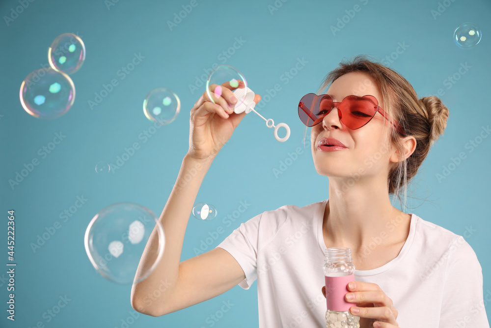 Young woman blowing soap bubbles on light blue background Young woman blowing soap bubbles on light blue background