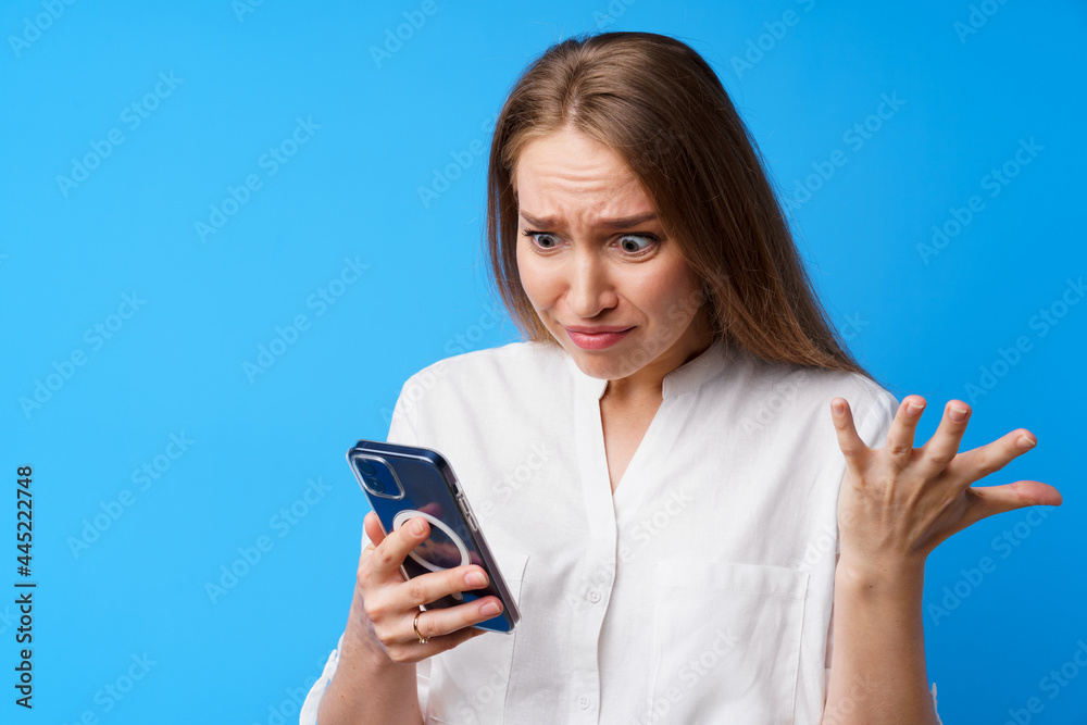 Portrait of young angry woman using her phone, annoyed texting with someone, blue background Portrait of young angry woman using her phone, annoyed texting with someone, blue background