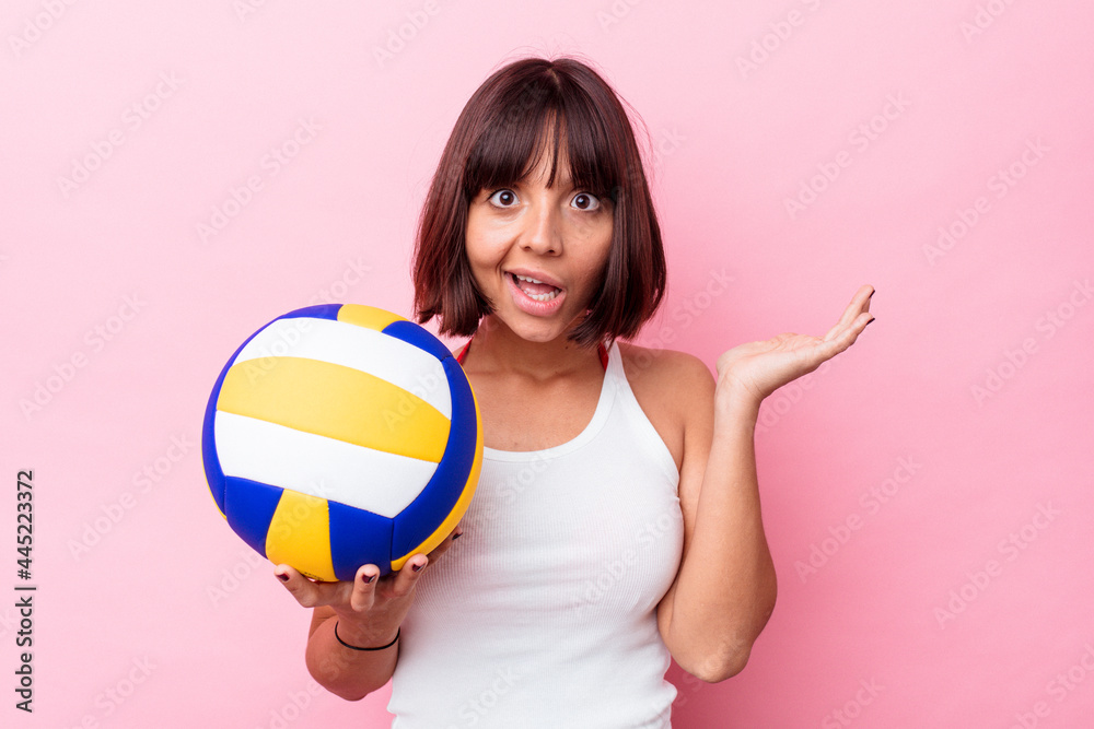 Young mixed race woman playing volleyball isolated on pink background surprised and shocked. Young mixed race woman playing volleyball isolated on pink background surprised and shocked.