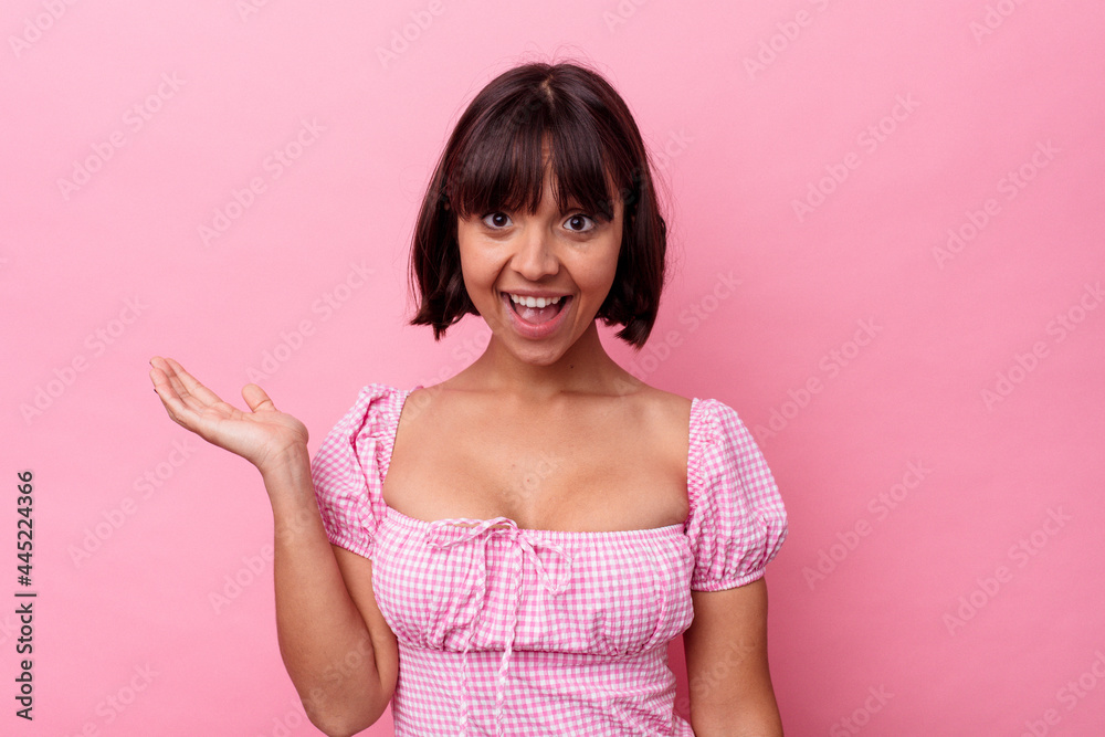 Young mixed race woman isolated on pink background showing a copy space on a palm and holding another hand on waist. Young mixed race woman isolated on pink background showing a copy space on a palm and holding another hand on waist.