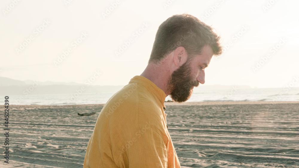 Hombre blanco barbudo sentado en playa al atardecer