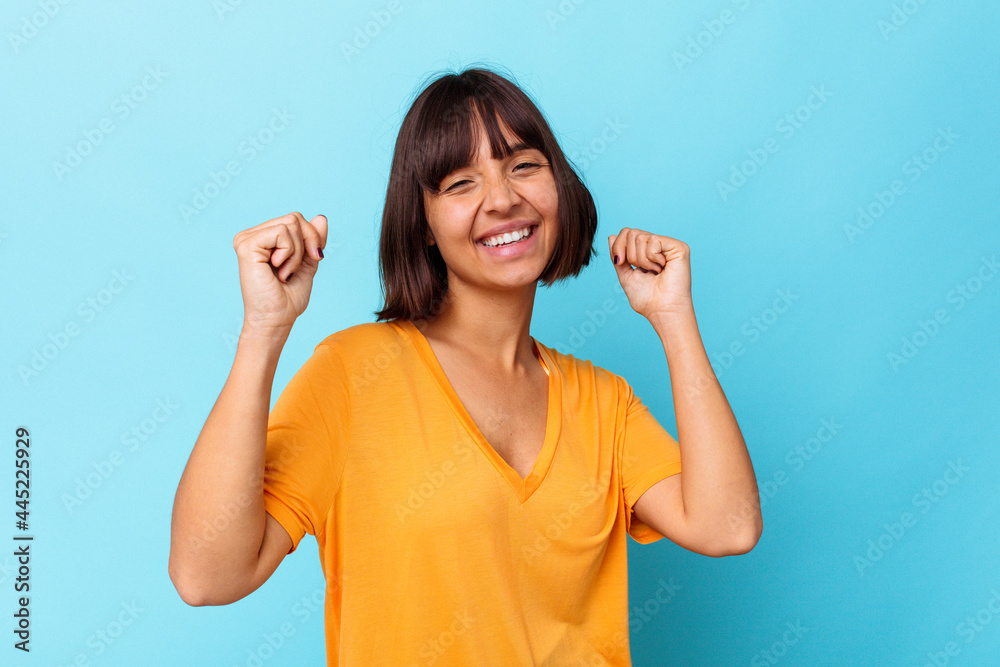 Young mixed race woman isolated on blue background celebrating a special day, jumps and raise arms with energy. Young mixed race woman isolated on blue background celebrating a special day, jumps and raise arms with energy.