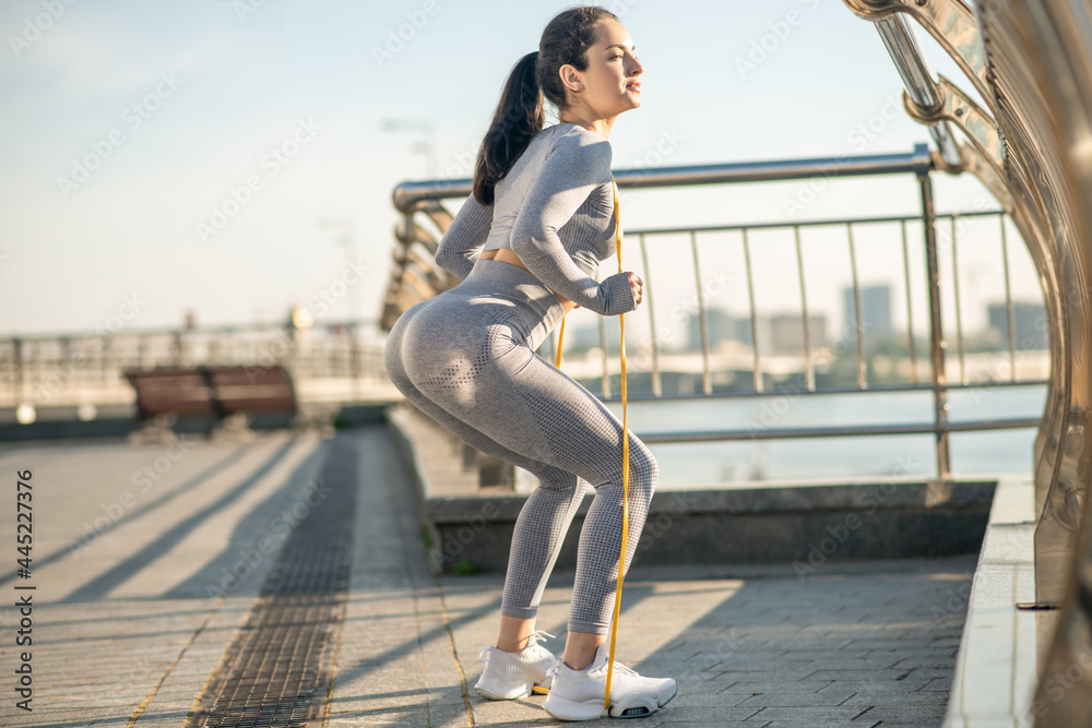 Young girl in grey sportswear having a workout with a resistance band