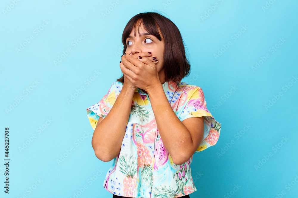 Young mixed race woman isolated on blue background thoughtful looking to a copy space covering mouth with hand. Young mixed race woman isolated on blue background thoughtful looking to a copy space covering mouth with hand.