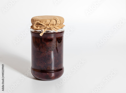 Homemade strawberry jam in a glass jar on a white background.