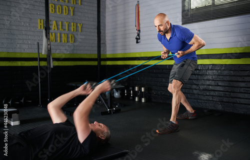 Personal trainer holding resistance bands. Mature man does bicep curl