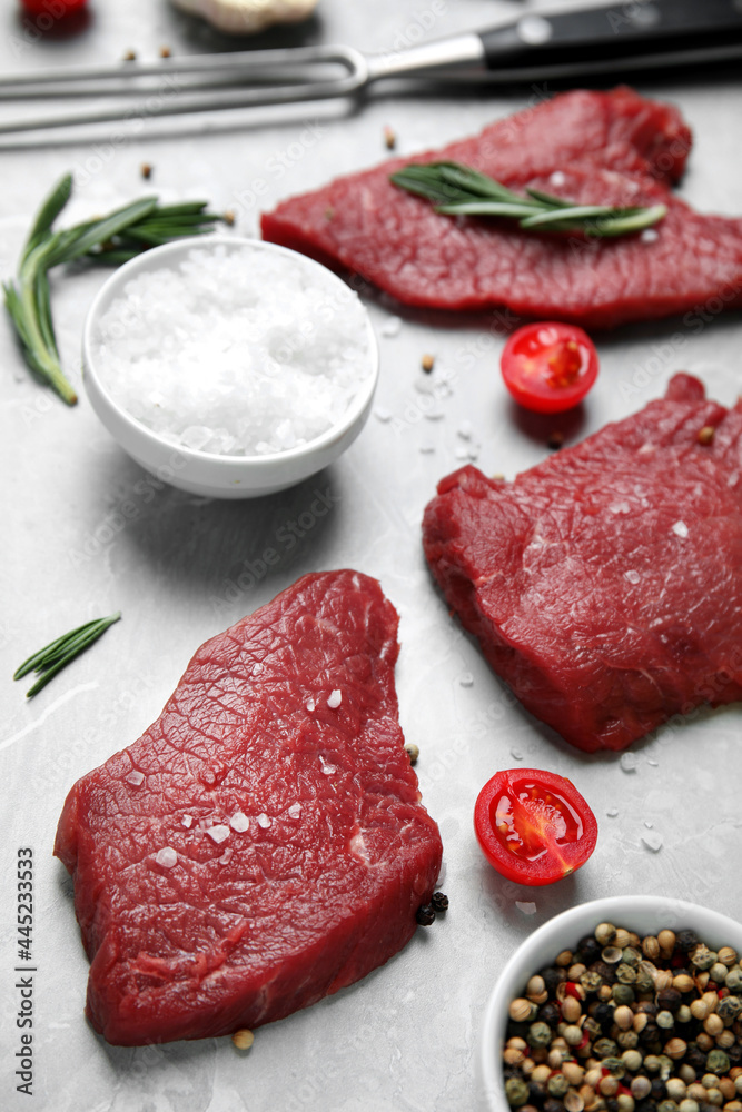 Fresh raw meat steaks and spices on light grey table
