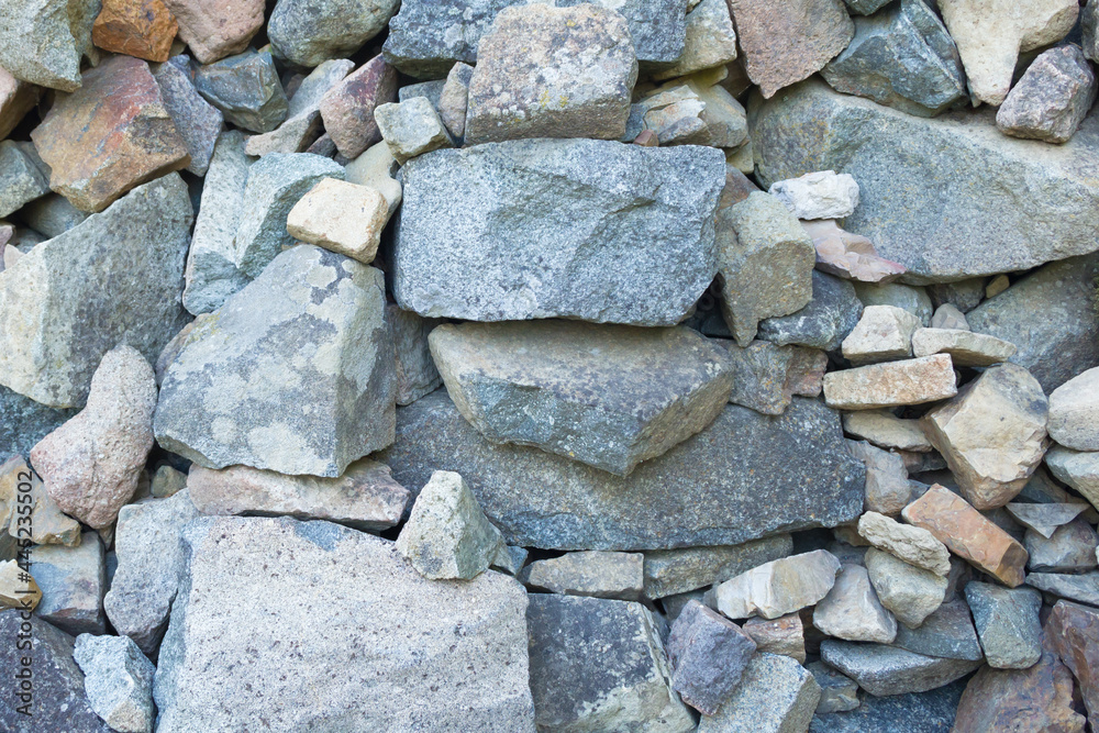 A pile, a heap of unprocessed granite stones of different sizes, shapes and colors, close-up. The stones are large, medium and small. The color is gray, brown, blue, brown. A pile, a heap of unprocessed granite stones of different sizes, shapes and colors, close-up. The stones are large, medium and small. The color is gray, brown, blue, brown.