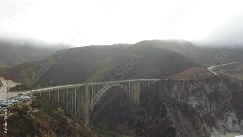 Cloudy aerial view of Bixby Bridge in Big Sur State Park in California. Vegetation and ocean waves can be seen along the coastline on Highway 1.