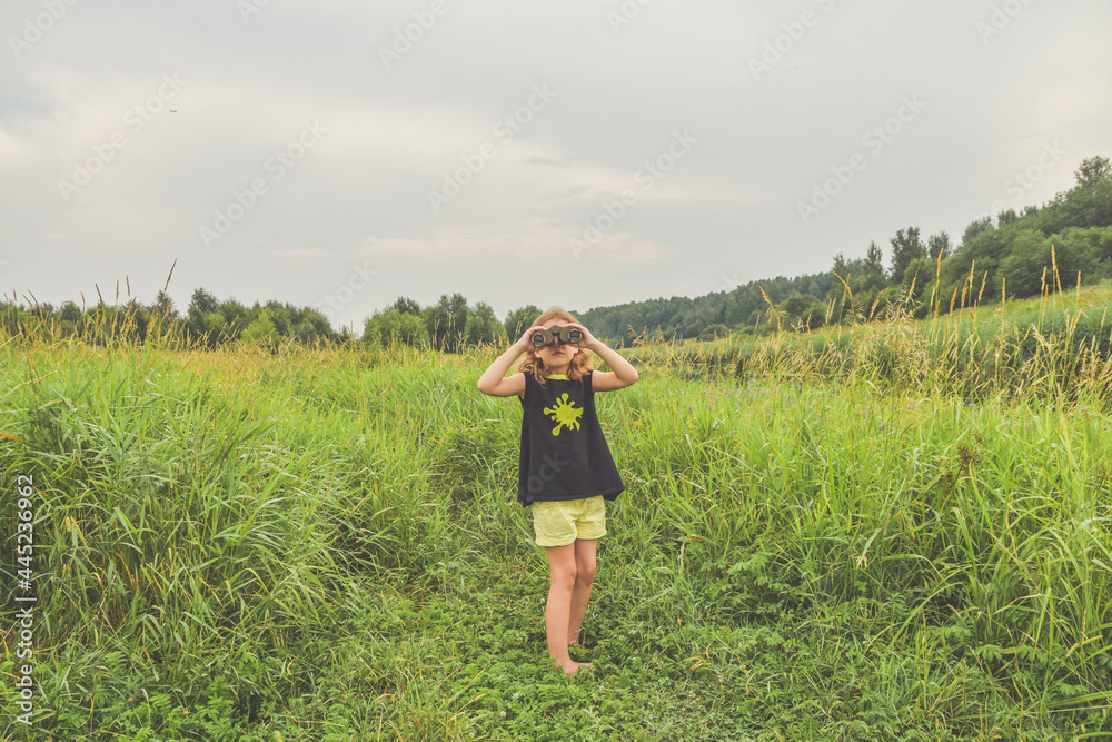 a child girl stands in a meadow and looks through binoculars