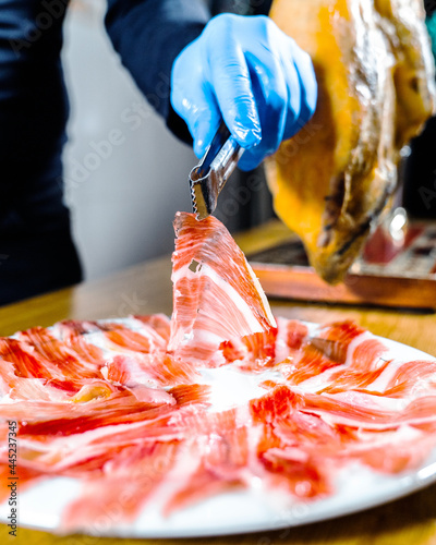 Ham plate. Appetizing traditional Spanish delicious slice Iberian jamón or cured ham leg. Person holding tweezers. Spanish gourmet food. Typical Spanish or Catalan food. Iberian pork.