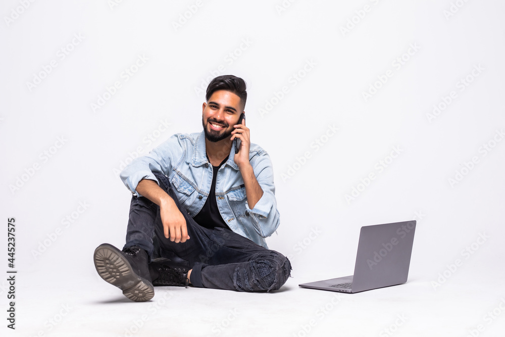 Young man sitting cross legged and talking on the phone while smiling to the camera isolated on white Young man sitting cross legged and talking on the phone while smiling to the camera isolated on white