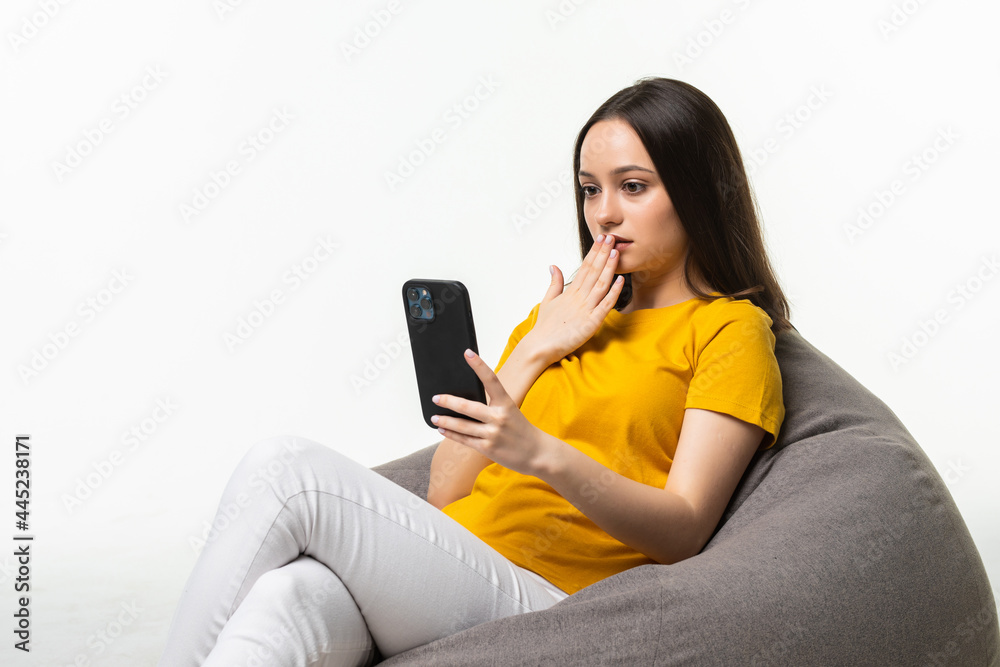 Young woman with mobile phone sitting on beanbag chair against on white background Young woman with mobile phone sitting on beanbag chair against on white background