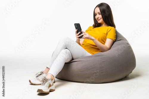 Young woman with mobile phone sitting on beanbag chair against on white background