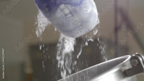 Pouring white powder from scoop in slow motion into mixing machine
