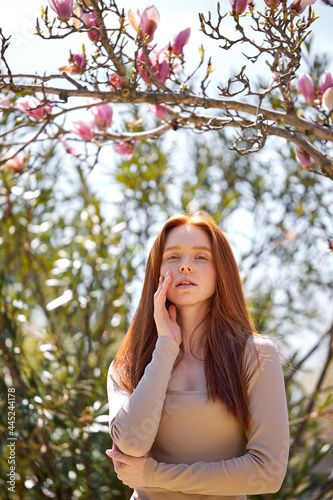 beautiful redhead female in blossoming garden touching face sensually, posing at camera. attractive woman with natural make-up enjoy time outdoors, in romantic beautiful place at spring © Roman
