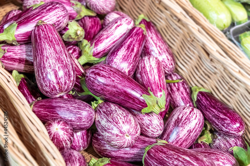 Purple striped eggplants in a wicker basket on a store shelf. Pockmarked texture of small lines and dots. Fresh vegetables at the grocery store. Purple graffiti eggplant. Selected focus, close-up