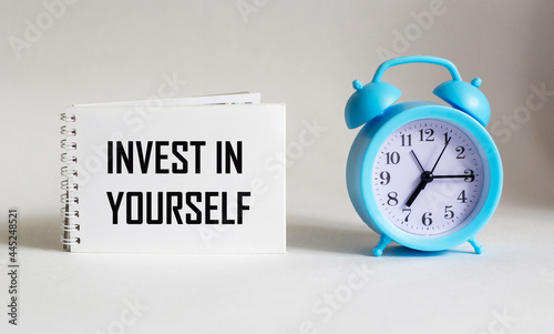 Invest in yourself, text is written on notepad and white background with alarm clock