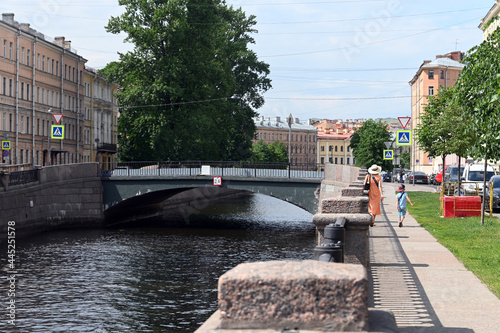 Bridges, canals and architecture of St. Petersburg. Embankment of the Griboyedov Canal, Kharlamov Bridge in the center of the old city of St. Petersburg. A woman in a hat and a child are walking along photo