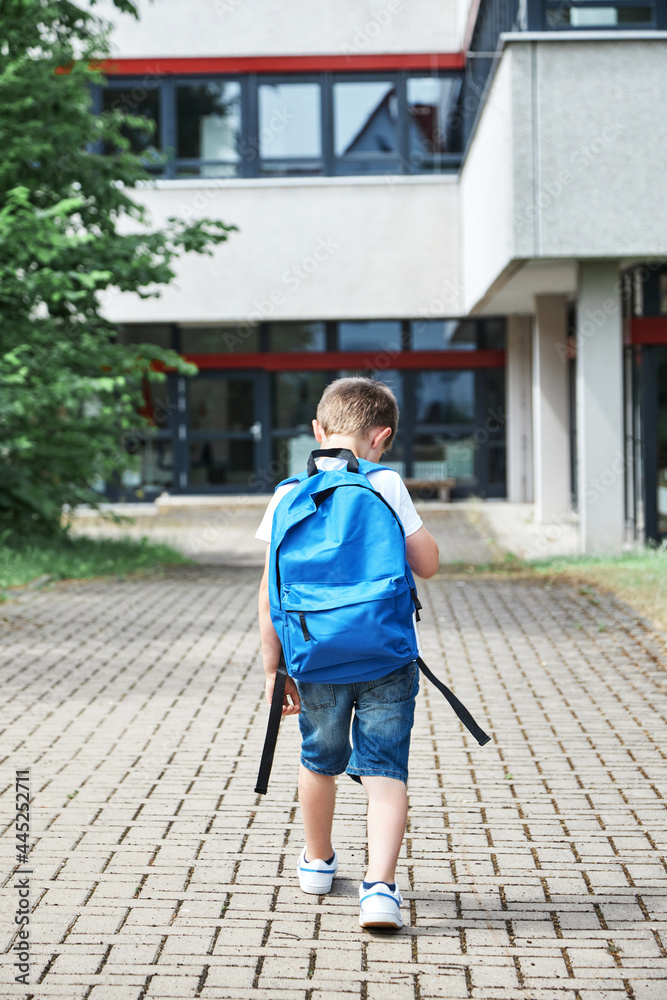 Back to school. Adorable Caucasian boy with blue backpack goes to school in first grade after summer vacation.