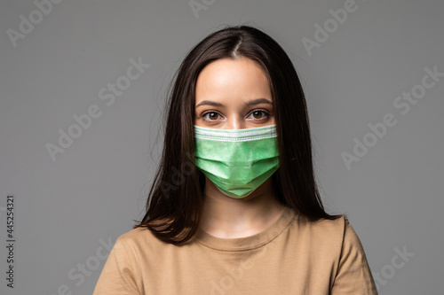 Portrait of a young woman in a medical mask isolated over grey background. Young girl patient stands against the wall background © dianagrytsku