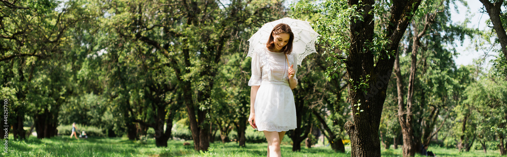 Smiling woman in dress holding umbrella in park, banner Smiling woman in dress holding umbrella in park, banner