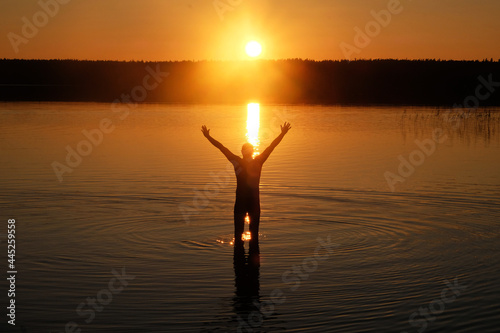Silhouette of a man with his hands raised in the water at sunset
