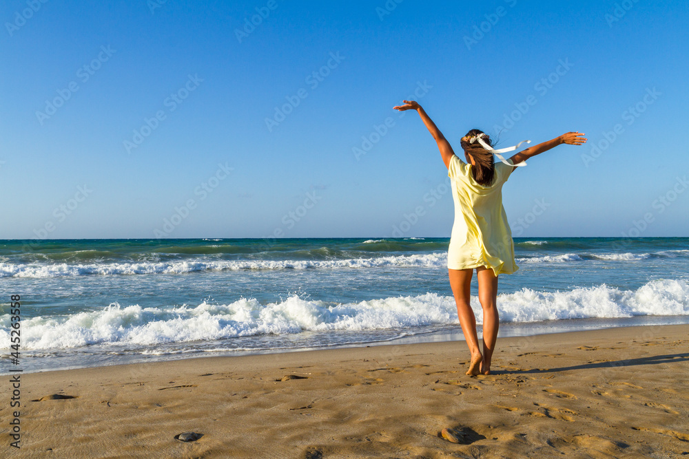 Beautiful carefree woman in short yellow dress enjoys freedom at the beach at dusk Beautiful carefree woman in short yellow dress enjoys freedom at the beach at dusk