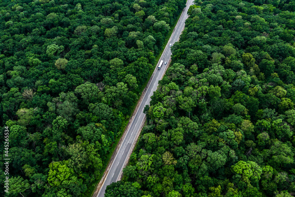 trucks carrying goods on the highway. white truck driving on asphalt road through a green forest. Drone top view seen from the air. Aerial view landscape. drone photography. cargo delivery. trucks carrying goods on the highway. white truck driving on asphalt road through a green forest. Drone top view seen from the air. Aerial view landscape. drone photography. cargo delivery.