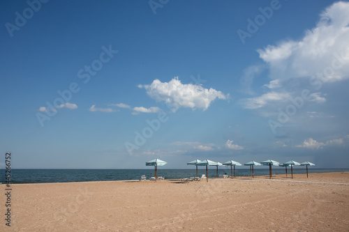 Sunshade, parasol, beach umbrella on sandy beach and sea background. Summer, travel, beach vacation concept. © Marharyta