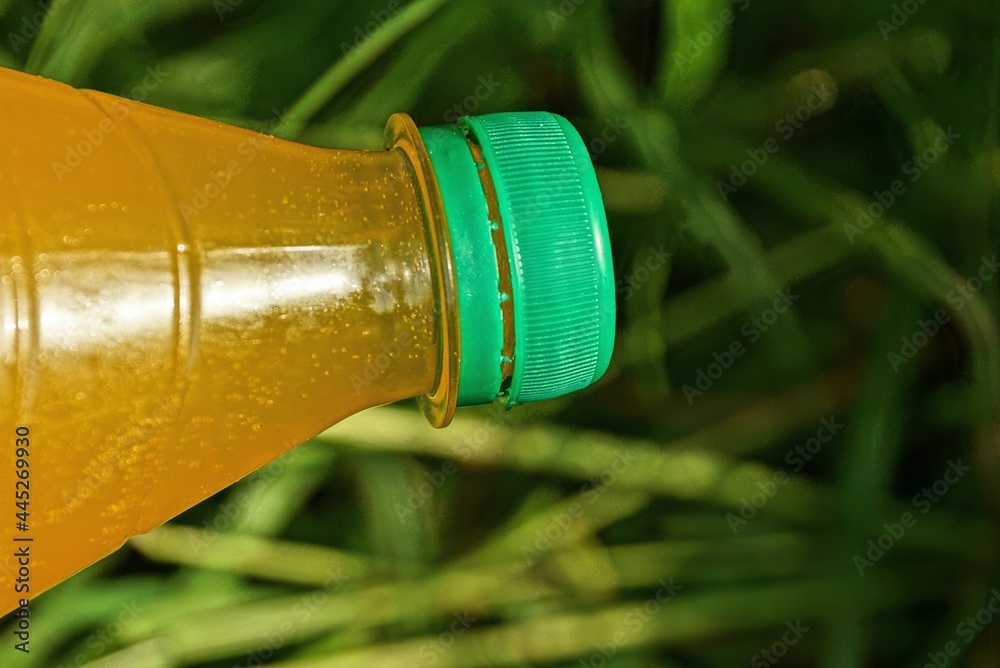 closed plastic bottle full of yellow lemonade on the background of green grass on the street closed plastic bottle full of yellow lemonade on the background of green grass on the street