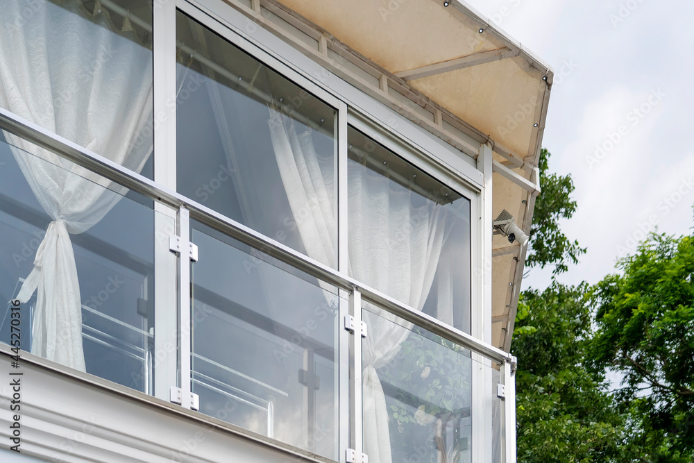 Fototapeta premium View of terrace with full-height windows from floor to ceiling, white curtains and canopy with trees in background