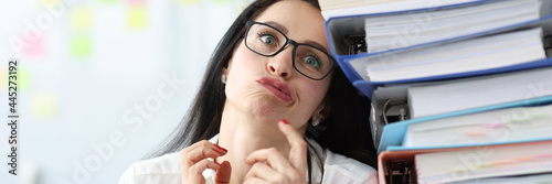 Tired businesswoman sits at her desk with large stack of folders with documents photo