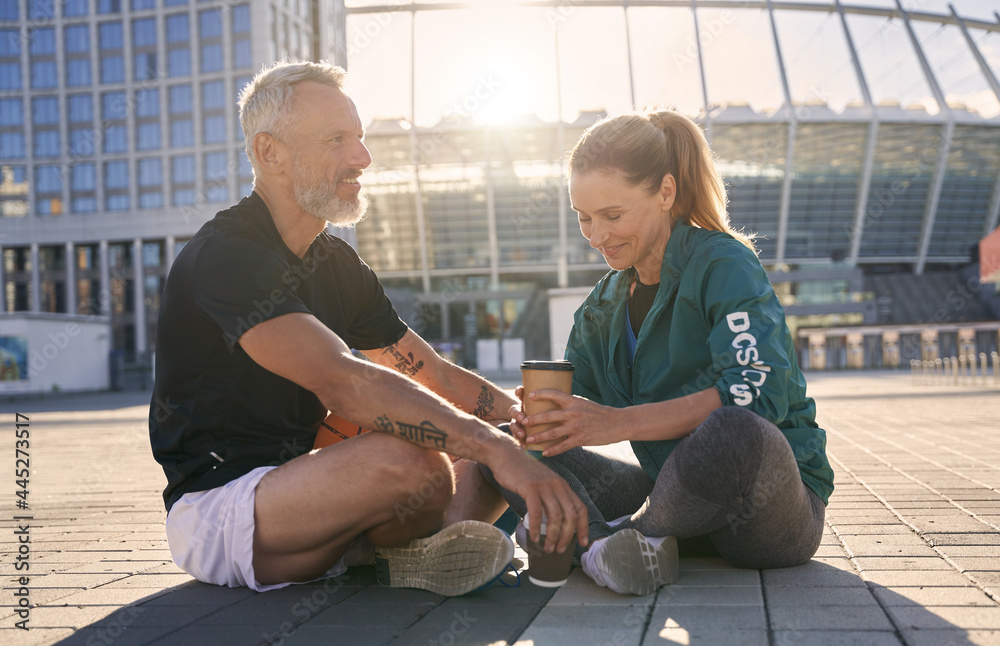 © Kostiantyn - Lovely mature couple in sportswear communicating with each other while drinking coffee, relaxing outdoors on a sunny summer day