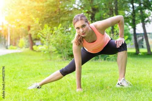fitness trainer woman warm up, stretching hands, legs, workout in park outdoors. sportive girl doing yoga exercises in park in sunny day. sports in city. female healthy sport lifestyle.
