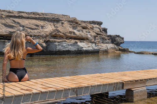 Blonde woman relaxing by the beach sitting on a wooden pier