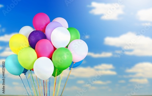 A bunch of multicolored balloons with helium on a blue sky and clouds background