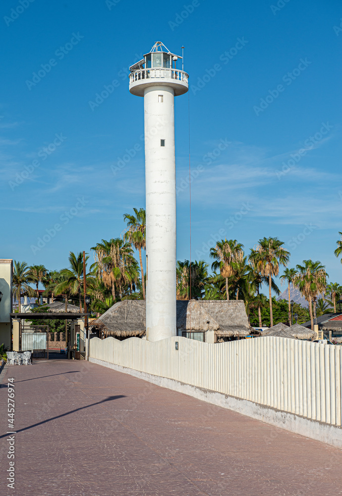 Vertical Lighthouse on the Malecon with palm trees and rocks in a sunny morning with blue calm water in the bay of Loreto in Baja California Sur. Mexico
