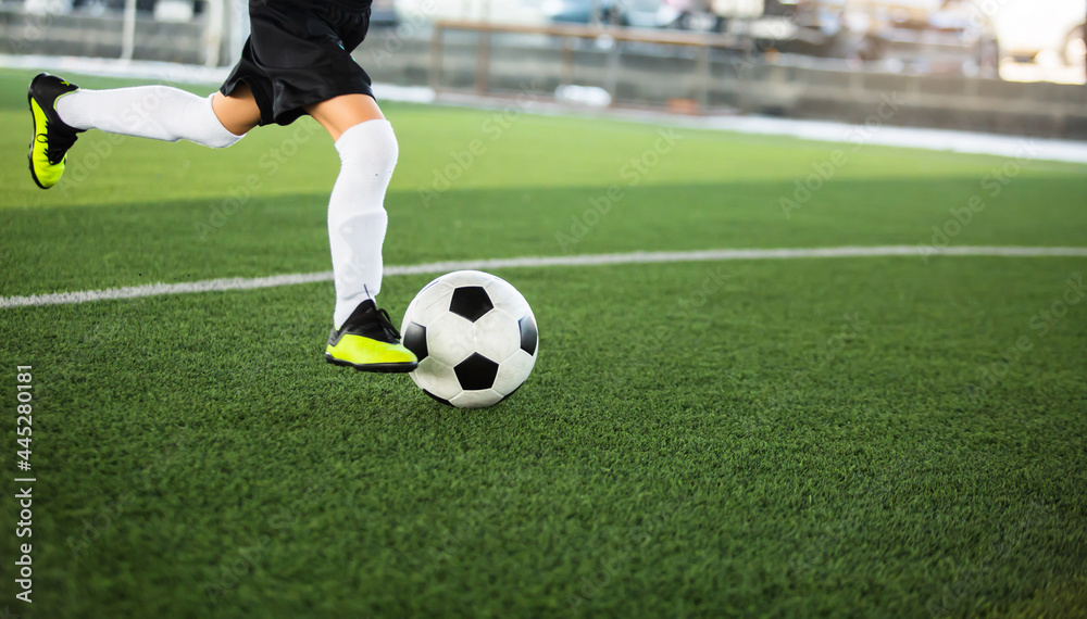 Selective focus to football with motion blur of kid soccer player shoot it on artificial turf. Soccer player training for football match.