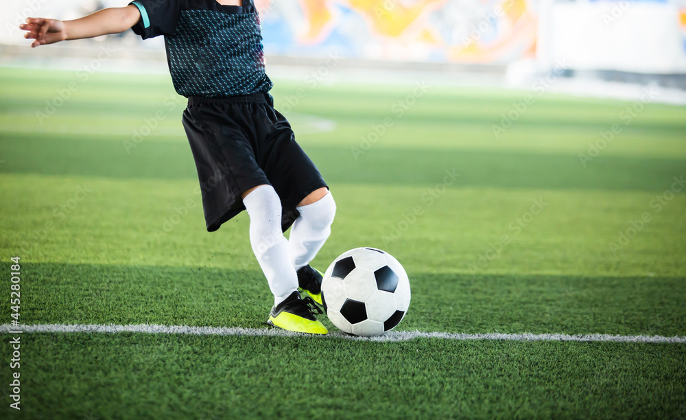 Selective focus to football with motion blur of kid soccer player shoot it on artificial turf. Soccer player training for football match. Selective focus to football with motion blur of kid soccer player shoot it on artificial turf. Soccer player training for football match.