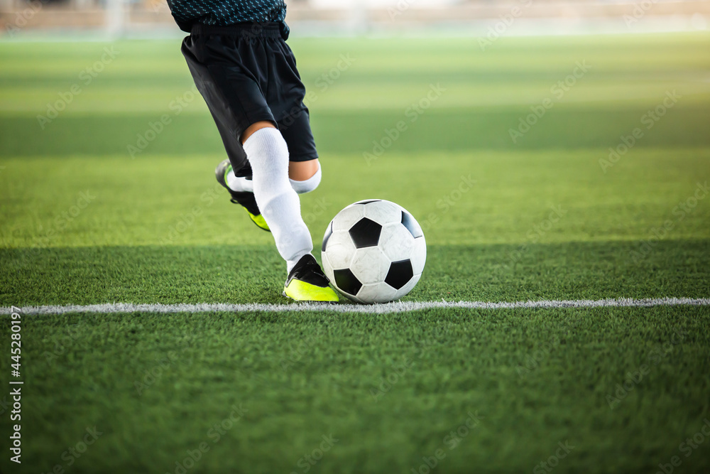 Selective focus to football with motion blur of kid soccer player shoot it on artificial turf. Soccer player training for football match.